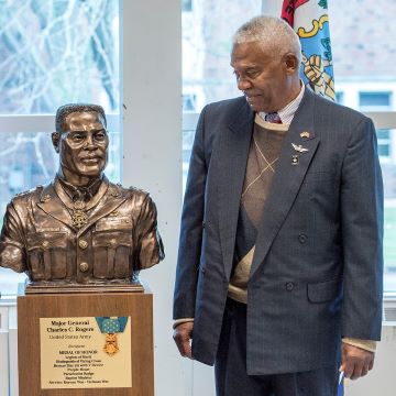 Photo showing ROTC Hall of Fame member smiling at a bronze statue